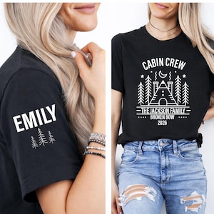 May include: Black t-shirts with white graphic designs. One shirt has the name "EMILY" on the sleeve with pine trees. The other shirt says "CABIN CREW" with a cabin graphic, family name, and the year 2026.