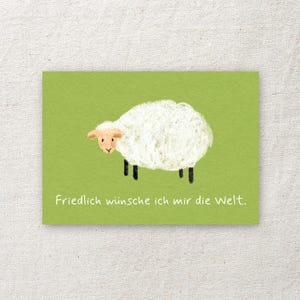Könnte beinhalten: Eine rechteckige Grußkarte mit hellgrünem Hintergrund und einer Illustration eines weißen, flauschigen Schafs. Das Schaf hat ein beiges Gesicht und schwarze Beine. Unter dem Schaf steht der weiße Text: Friedlich wünsche ich mir die Welt.