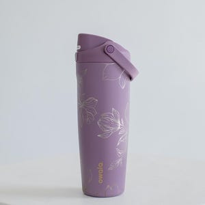 Op de afbeelding: Een paarse geïsoleerde waterfles met een klapdeksel en handvat. De fles is versierd met een zilveren bloemenpatroon. De merknaam "owala" staat op de zijkant. De fles staat op een wit oppervlak.