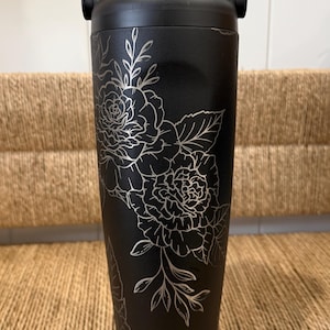 Peut inclure: Gobelet isotherme noir avec un motif floral argenté. Le gobelet a une poignée et un couvercle noirs. Le motif floral présente des roses et des feuilles. Conçu pour garder les boissons froides ou chaudes.