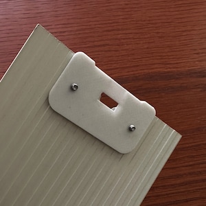 May include: A white plastic bracket with two silver screws attached to a textured, light gray surface.