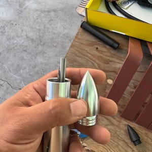 Puede incluir: Una herramienta de soldadura de metal desmontada con un acabado plateado. La herramienta tiene un cuerpo cilíndrico y una punta cónica. La imagen muestra los componentes de la herramienta, incluida la punta y el cuerpo principal, sostenidos en una mano.