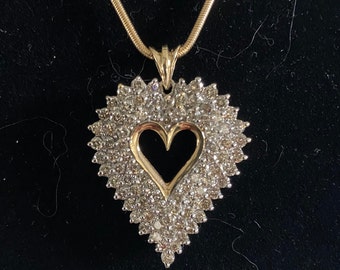 Puede incluir: Un collar de cadena de oro con un colgante en forma de corazón incrustado con pequeños diamantes.