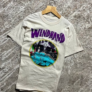 May include: A white t-shirt with a purple graphic of the word "WINDHAND" and a black and white illustration of a figure with a crown and a woman lying down.