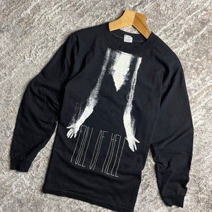 Op de afbeelding: Zwart longsleeve shirt met een witte afbeelding van een persoon met uitgestrekte armen en de tekst "Full of Hell" eronder.