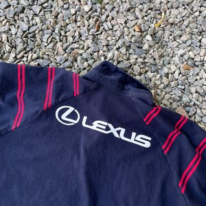 Peut inclure: Veste noire &agrave; fermeture &eacute;clair avec des rayures rouges et un logo "LEXUS" blanc au dos.