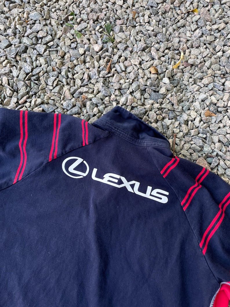 Peut inclure: Veste noire &agrave; fermeture &eacute;clair avec des rayures rouges et un logo "LEXUS" blanc au dos.