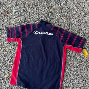 Peut inclure: Un t-shirt &agrave; manches courtes ray&eacute; noir et rouge avec un logo "LEXUS" blanc au dos.