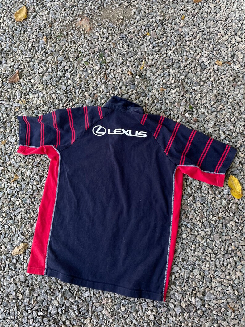 Peut inclure: Un t-shirt &agrave; manches courtes ray&eacute; noir et rouge avec un logo "LEXUS" blanc au dos.