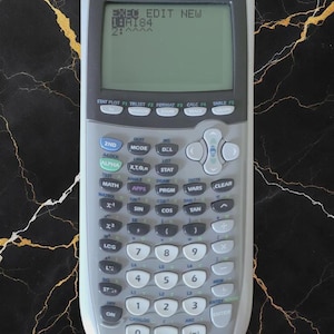 May include: A TI-84 Plus Silver Edition calculator with a gray and silver design. The screen displays text including "EDIT NEW" and "18AI84". The calculator has numerous buttons for various functions, including math, trig, and graphing.