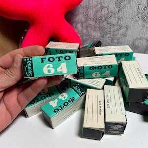 Puede incluir: Un montón de botes de película vintage con etiquetas verdes y blancas. Las etiquetas dicen "FOTO 64" y "Svema".