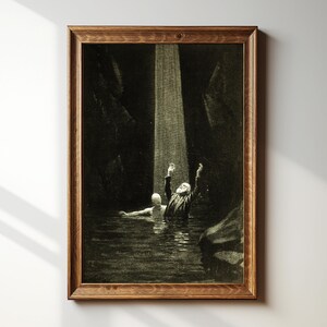 May include: A framed sepia-toned print depicts a man in a suit with arms raised in water, illuminated by a beam of light. Another figure floats nearby. The artwork is set in a dark, cavernous environment, framed in a wooden border.