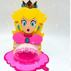 Peut inclure: Un personnage de Princess Peach rose et jaune de la série de jeux vidéo Super Mario Bros. Le personnage tient un dôme en plastique transparent avec une base rose. Le dôme est conçu pour contenir des bonbons ou de petites friandises. Le personnage mesure 8 cm (3,15 pouces) de haut.