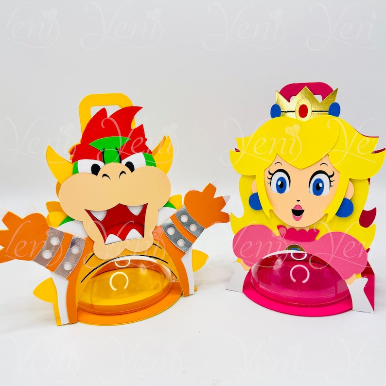Puede incluir: Dos recortes de papel hechos a mano y coloridos de personajes de videojuegos. Uno es Bowser, con detalles naranjas, amarillos, rojos y verdes. La otra es la Princesa Peach, con cabello amarillo, un vestido rosa y una corona. Ambos tienen recipientes de pl&aacute;stico transparente.