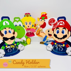 Puede incluir: Soportes de caramelos coloridos con personajes de una popular serie de videojuegos. Los soportes tienen forma de Mario, Luigi, Yoshi, Princesa Peach y Toad. Cada soporte tiene un recipiente redondo y transparente. El texto "Candy Holder" y "8cm / 3.15" spheres" es visible.