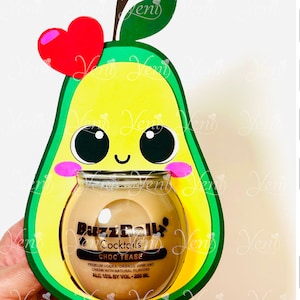 May include: A green avocado-shaped cardstock cutout with a smiling face and a heart on top. Inside the avocado is a clear glass jar with a brown liquid and the text "BuzzBall Cocktails CHOC TEASE" on the label. The jar is 200 ml and has an alcohol content of 15%.