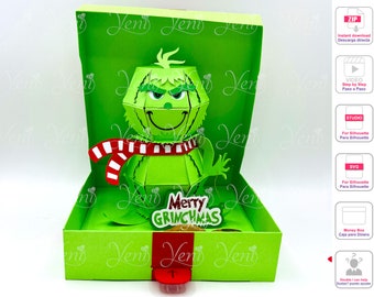 Puede incluir: Una tarjeta emergente verde con el Grinch de la película "El Grinch". El Grinch lleva una bufanda a rayas rojas y blancas y sostiene un cartel que dice "Merry Grinchmas".