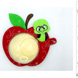 Puede incluir: Una manzana roja con un gusano verde en la parte superior. La manzana tiene una ventana de plástico transparente en el centro. El gusano tiene una cara negra con ojos blancos y una pequeña sonrisa. La manzana tiene un diámetro de 8 cm.