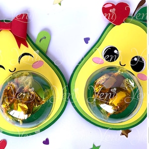 May include: Two avocado-shaped paper crafts with cute faces, each with a clear plastic dome containing chocolate candies. The avocado on the left has a red bow on top. The image includes text for instant download, step-by-step video, and silhouette studio files.