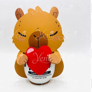 May include: A brown cartoon llama holding a red heart in its paws. The llama is holding a bottle of pineapple flavored alcoholic beverage. The bottle is labeled "PINEA LADA" and has a white label with black text. The image is a digital download for use with a Silhouette cutting machine.
