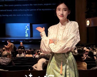 Pode incluir: Uma mulher com uma blusa branca e uma saia verde está em frente a uma plateia. A saia tem um padrão floral e uma borla. A imagem inclui o texto "诗衣图 SILKY ECHO" na parte inferior.