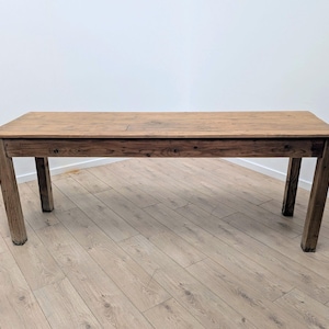 May include: A rectangular wooden table with a natural finish. The table has four sturdy legs and a long, flat surface. The wood grain is visible, adding to its rustic charm. The table is approximately 183 cm long and 91 cm wide.