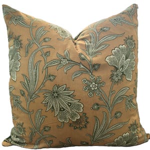 May include: A square decorative pillow with a floral pattern. The pillow features a tan background with a repeating design of green and white stylized flowers, leaves, and vines. The pillow is made of a soft fabric and is likely used for home decor.