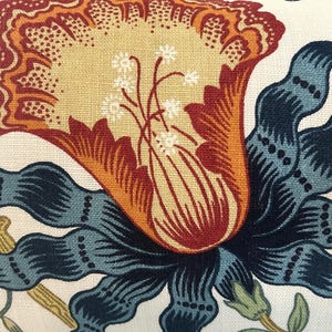 Może przedstawiać: Tkanina z dużym, stylizowanym wzorem kwiatowym na kremowym tle. Kwiat ma wyraźny, ż&oacute;łto-pomarańczowy środek w kształcie trąbki z białymi pręcikami, otoczony ciemnoniebieskimi, falistymi liśćmi i łodygami przypominającymi płatki.