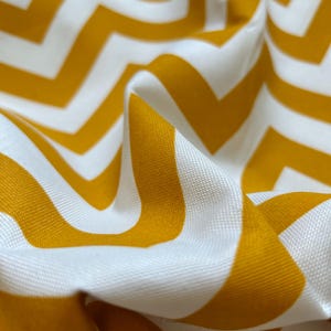 May include: White and yellow chevron patterned fabric. The fabric is folded and has a soft, textured surface.