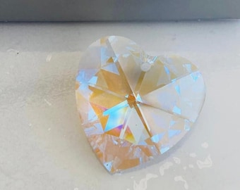 May include: A clear crystal heart-shaped pendant with iridescent rainbow colors. The pendant has a hole at the top for hanging. The pendant is made by Swarovski.