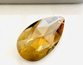 May include: A teardrop-shaped crystal pendant in a golden amber color. The crystal is faceted and has a high shine. The pendant is made by Swarovski.