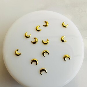 Può includere: Una collezione di 12 ciondoli per unghie a forma di mezzaluna dorati. I ciondoli sono piccoli e delicati, perfetti per aggiungere un tocco di fantasia alla tua nail art.