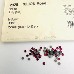 May include: A close-up of a small package of 1,440 ruby red Xilion Rose Swarovski crystals, size 10, with M-Foiled Hotfix. The package is labeled with the product number 2028.