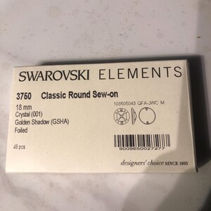 May include: A package of 48 gold-toned sew-on crystals, labeled "Swarovski Elements 3750 Classic Round Sew-on 18 mm Crystal (001) Golden Shadow (GSHA) Foiled".