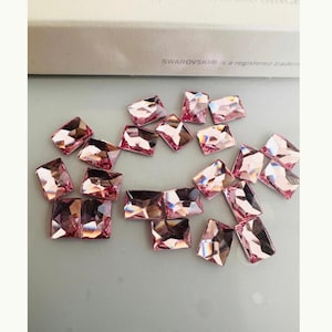 Könnte beinhalten: Eine Sammlung von rosa rechteckigen Strasssteinen. Die Strasssteine sind auf einer weißen Oberfläche verstreut. SWAROVSKI® ist eine eingetragene Marke.