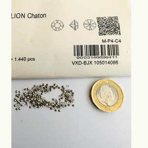 May include: A close-up of a pile of small, clear, round rhinestones with a silver backing. The rhinestones are scattered on a white surface. A British one pound coin is in the background for scale.