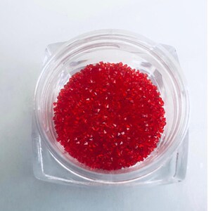 Puede incluir: Un pequeño recipiente transparente lleno de brillantes piedras de cristal rojo brillante y facetadas.