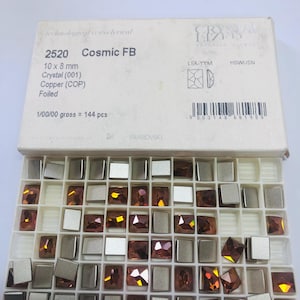 May include: A white cardboard box containing 144 pieces of 10 x 8 mm Swarovski 2520 Cosmic FB crystals in a copper color. The box lid features the text 'CRYSTALIZED', '2520 Cosmic FB', '10 x 8 mm', 'Crystal (001)', 'Copper (COP)', and 'Foiled'.
