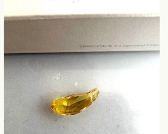 May include: A small, yellow crystal charm in the shape of a teardrop. The charm is made by Swarovski.