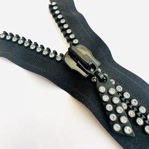 May include: Black zipper with clear rhinestone embellishments. The zipper pull is black plastic with a silver finish.