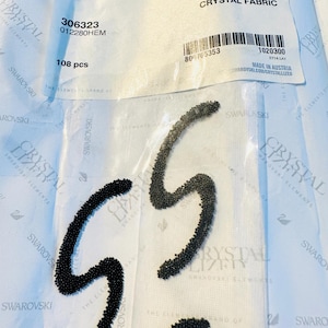 Puede incluir: Tela de cristal negro con un diseño ondulado. La tela está hecha de 108 pequeños cristales negros. El embalaje incluye el código de producto 306323, 012280HEM y el texto "Crystal Fabric".