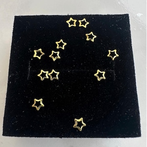 May include: A black velvet display case with 11 gold star-shaped charms arranged in a constellation pattern.