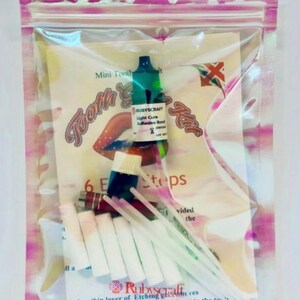 May include: A clear plastic bag containing a mini tooth gem kit. The kit includes a small bottle of light cure adhesive bond, a small bottle of blue liquid, a small bottle of green liquid, six small white cotton swabs, and two white plastic applicators. The bag also includes a printed instruction sheet with the text "Mini Tooth Gem Kit" and "6 Easy Steps".