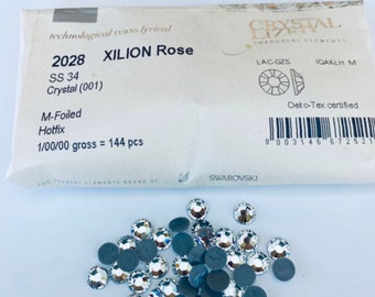 May include: A close-up of a package of 144 clear crystal Xilion Rose rhinestones, size SS 34, with a silver foil backing. The rhinestones are labeled as "M-Foiled Hotfix" and are part of the Swarovski Crystal Elements brand.