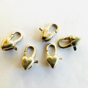 Könnte beinhalten: Fünf silberne herzförmige Verschlüsse zum Schmuckmachen. Jeder Verschluss hat einen federbelasteten Mechanismus zum einfachen Öffnen und Schließen.