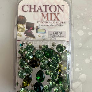 Puede incluir: Un paquete de piedras de Chaton Mix verdes con parte posterior puntiaguda en varios tamaños y colores. El paquete dice "Crea tu estilo" con elementos de Swarovski.