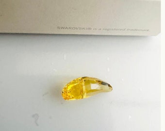 May include: A yellow crystal in the shape of a teardrop. The crystal is faceted and has a shiny finish.