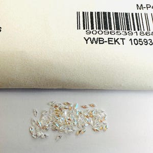 May include: A pile of small, clear, faceted, marquise-shaped crystals. The crystals have a rainbow iridescent effect.
