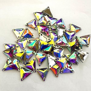 Puede incluir: Un montón grande de piedras de cristal triangulares iridiscentes. Las piedras de cristal tienen un efecto arcoíris y están esparcidas sobre una superficie blanca.