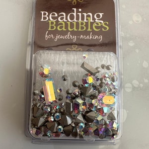Puede incluir: Un paquete de plástico transparente que contiene una variedad de cuentas de vidrio iridiscentes y piedras de imitación. El paquete está etiquetado como "Beading Baubles for jewelry-making".